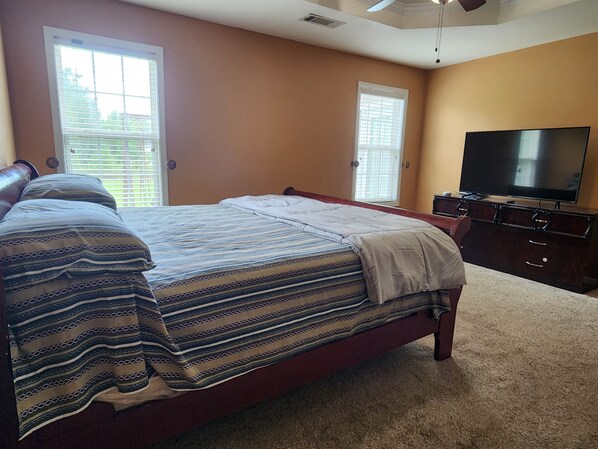 A bedroom with a large bed, a television, and two windows with blinds.