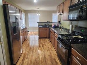 A kitchen with wooden cabinets, a stainless steel refrigerator, a microwave, a stove, and a water dispenser.