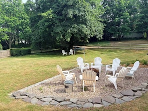 An outdoor seating area with Adirondack chairs arranged around a central fire pit, surrounded by a stone border. - Spacious pet-friendly home, close to Nauset & Skaket beaches and Orleans village (Orleans)