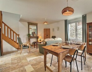 A dining area with a wooden table and chairs, a staircase, and a view of the outdoors through large windows. - La Terre Chérie - LAMBALLE-ARMOR (LAMBALLE-ARMOR)