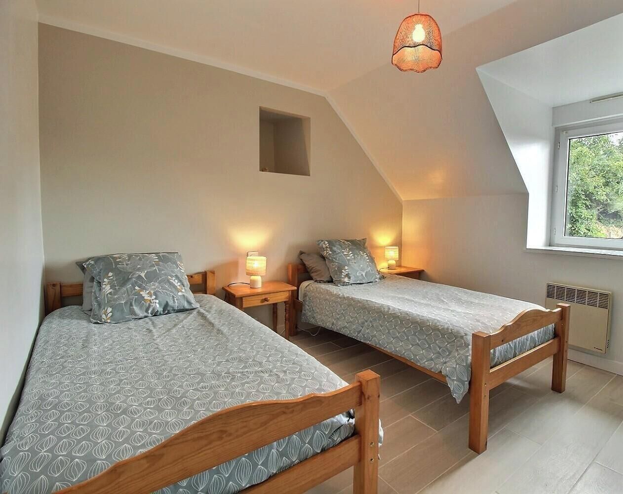 Een slaapkamer met twee houten bedden, nachtkastjes en een plafondlamp.