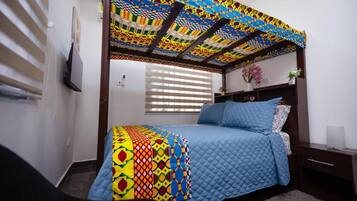 A bedroom with a bed, a nightstand, a window with blinds, and a colorful ceiling.