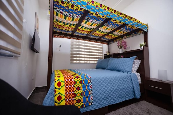 A bedroom with a bed, a nightstand, a window with blinds, and a colorful ceiling.