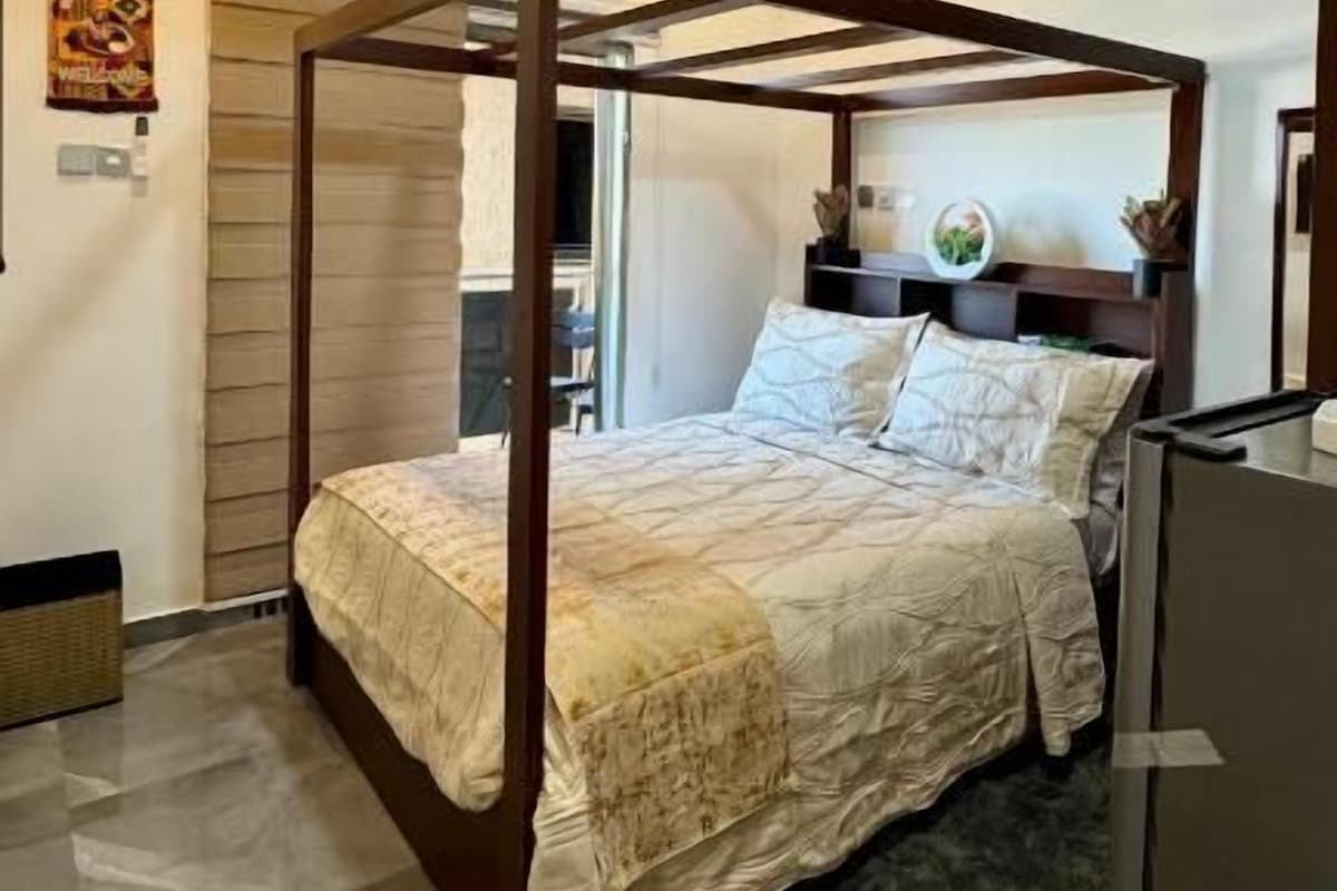 Una cama con dosel y dosel beige, un ventilador de techo y una mesita de noche con una lámpara.