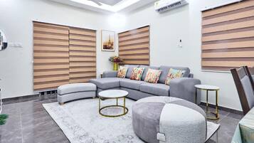 Un salon moderne avec un canapé d’angle, des poufs ronds, une table basse et un tapis à motifs.