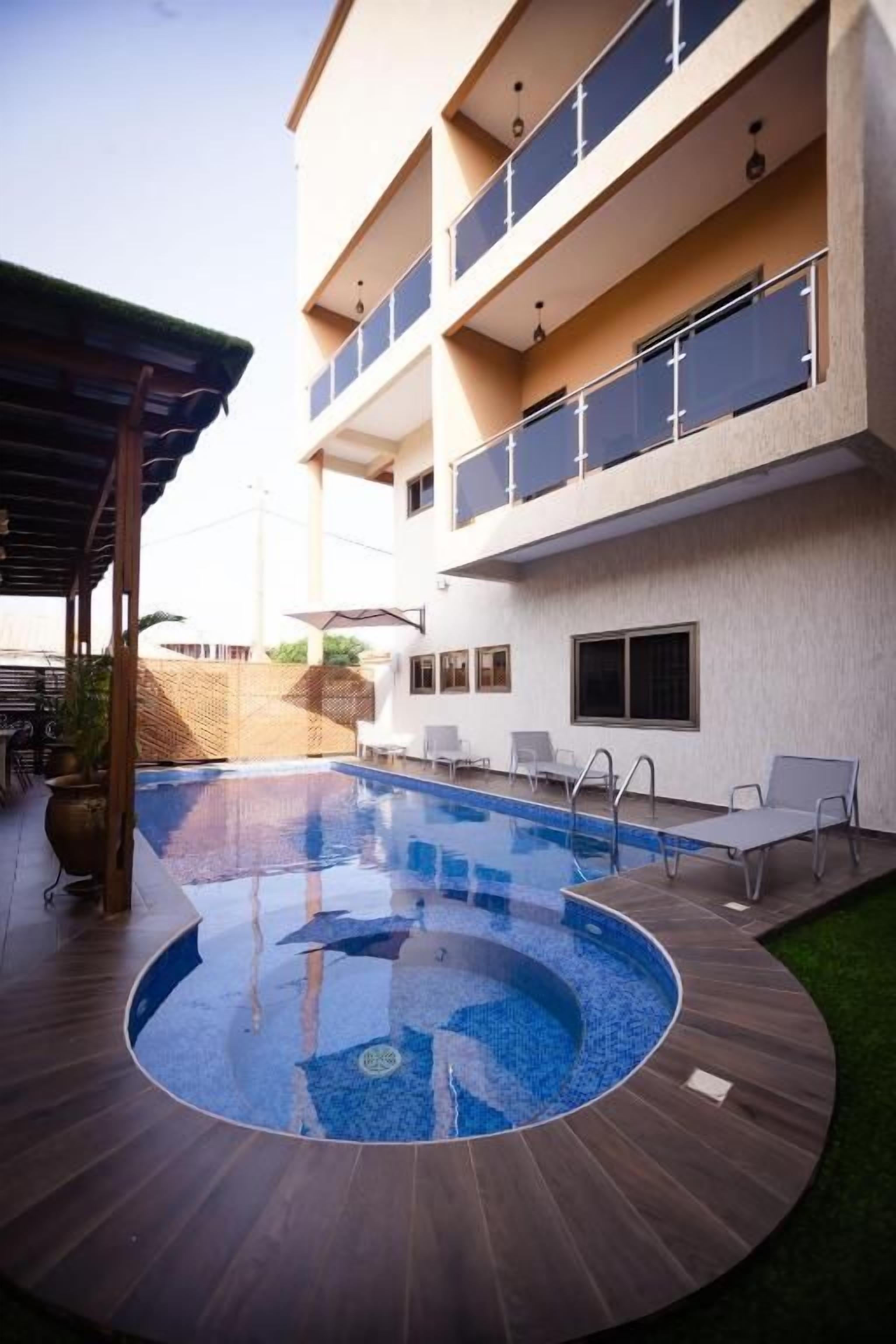 Une piscine dotée d’une terrasse en bois, d’un espace couvert et d’un bâtiment avec des balcons.