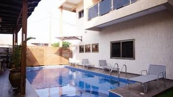 Une piscine dotée d’une terrasse en bois, d’un espace couvert et d’un bâtiment avec des balcons.