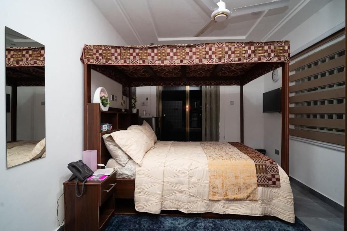 Una cama con dosel y cuatro columnas, una mesita de noche con un teléfono y una lámpara, y una alfombra azul.