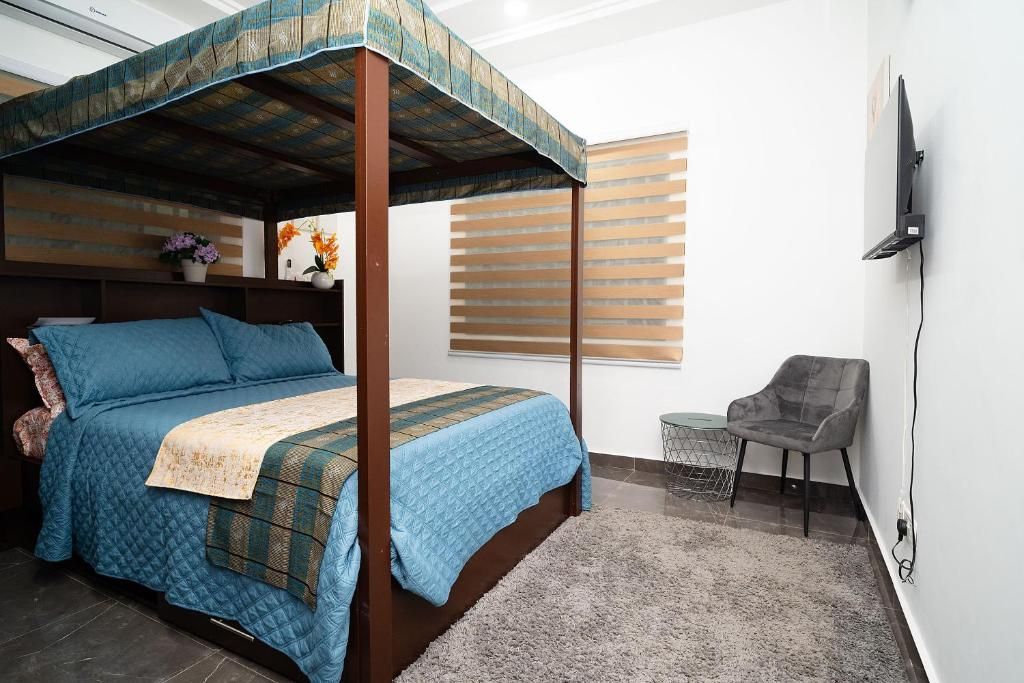 A bedroom with a four-poster bed, a television mounted on the wall, and a small table with a chair.