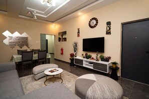 A modern living room with a flat-screen TV, a dining area with chairs, a sofa, and a coffee table. - Cherry Signature Condos (Adenta Municipality)