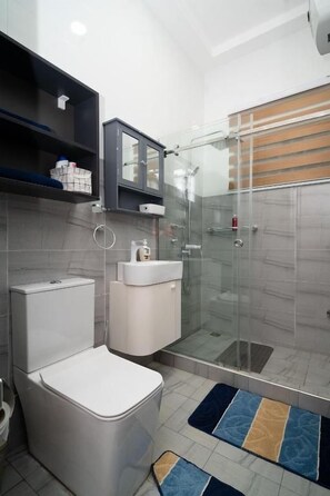 Un baño moderno con inodoro, lavamanos y cabina de ducha de vidrio.