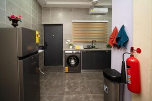Een kleine keuken met een koelkast, wasmachine, gootsteen en een brandblusser.