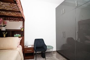 A bedroom with a bed, a desk, a chair, a wardrobe, and a shelf with decorative items. - Cherry Signature Condos (Adenta Municipality)