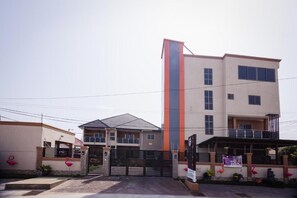 A multi-story building with a prominent vertical stripe, a gated entrance, and flamingo statues. - Cherry Signature Condos (Adenta Municipality)