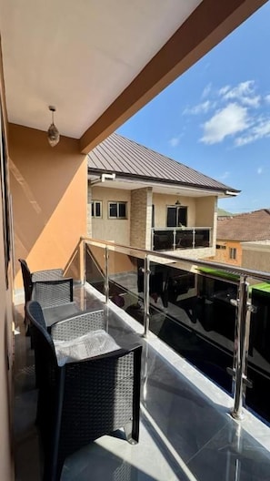 A balcony with a glass railing, a table, and chairs. - Cherry Signature Condos (Adenta Municipality)