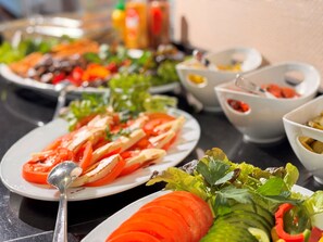 A buffet table with various dishes including sliced tomatoes, cucumbers, and leafy greens. - Hotel Rhein-ruhr (Bottrop)
