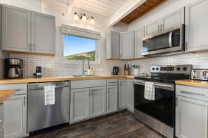 A modern kitchen with grey cabinets, stainless steel appliances, a wooden countertop, and a window with a view of greenery. - Apres Ski House - Pet Friendly, Perfect for Couples, Small Families (Steamboat Springs)