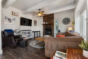A living room with a fireplace, a television, a clock, and a ceiling fan. - Apres Ski House - Pet Friendly, Perfect for Couples, Small Families (Steamboat Springs)