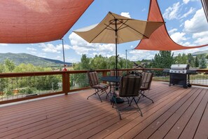 A wooden deck with a table and chairs, a grill, and a view of a mountainous landscape. - Apres Ski House - Pet Friendly, Perfect for Couples, Small Families (Steamboat Springs)
