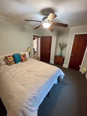 A bedroom with a large bed, a ceiling fan, and a door leading to another room.