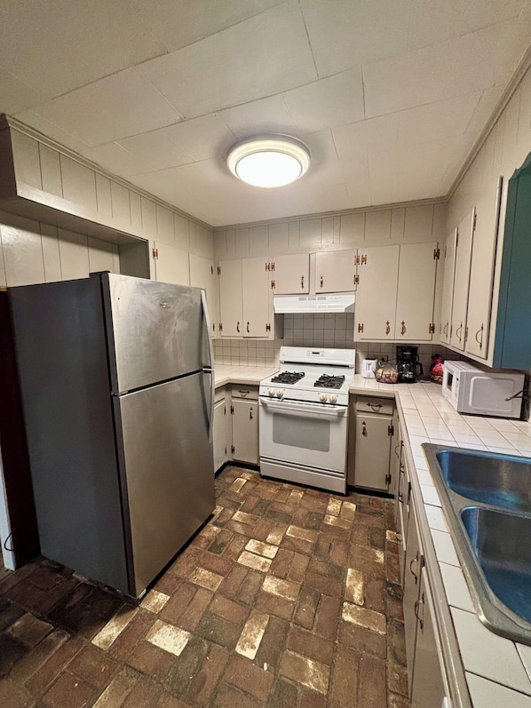 A kitchen with white cabinets, a stainless steel refrigerator, a stove, and a microwave.
