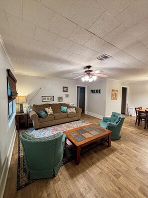 A living room with a brown sofa, teal armchairs, a wooden coffee table, and a ceiling fan.