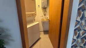 Uma área de lavanderia compacta, com máquina de lavar, pia pequena e aquecedor de água.