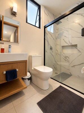 Ein modernes Badezimmer mit einer Duschkabine aus Glas, einer Toilette und einem Waschtisch mit Spiegel.