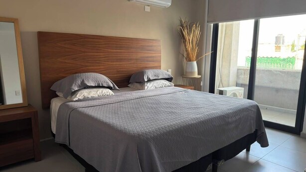 Quarto moderno com uma cama grande, cabeceira de madeira e vista para o exterior através de uma porta de correr de vidro.