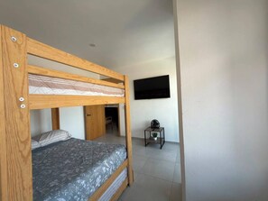 Ein Zimmer mit einem Etagenbett, einem kleinen Tisch mit einer Pflanze und einem an der Wand montierten Fernseher.