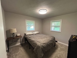 A bedroom with a bed, two windows, a lamp, and a desk.
