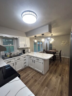 A modern kitchen with white cabinets, a central island, and a dining area with a table and chairs. - Notre Dame stadium 17 mins. Sleeps 6 “ 5 star host” (South Bend)
