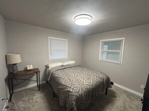 A bedroom with a bed, two bedside tables, a lamp, and two windows with blinds. - Cozy Brick Home 17 Min to ND. Sleeps 6 “ 5 star host” (South Bend)