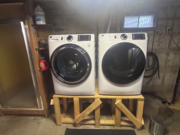 Two front-loading washing machines on wooden stands in a utility room.