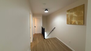 A hallway with wooden flooring, a white door at the end, and a black railing. - Excellent 3-bedroom house with AC in cool Louisville neighborhood (Louisville)