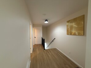 A hallway with wooden flooring, a white door at the end, and a black railing. - Excellent 3-bedroom house with AC in cool Louisville neighborhood (Louisville)