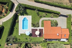 Ein Luftbild eines Grundstücks mit Swimmingpool, einem Gebäude mit rotem Dach und gepflegten Gärten.