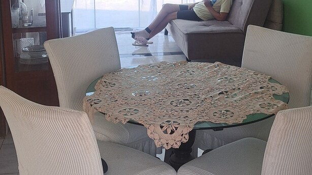 Ein Wohnzimmer mit Glastisch, weißen Stühlen, einer Couch und einer entspannten Person.