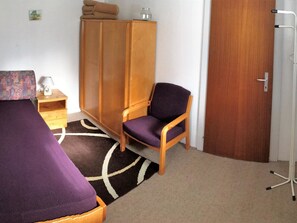 A room with a bed, a chair, a wardrobe, a nightstand, and a door. - Chalet Waldesruh (3 ZWhg.) Appartement/Fewo, Badewanne, Komfort 4-Bettwohnung by Interhome (Arosa)
