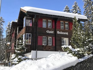 A chalet with a wooden facade and red shutters, surrounded by snow-covered trees. - Chalet Waldesruh (3 ZWhg.) Appartement/Fewo, Badewanne, Komfort 4-Bettwohnung by Interhome (Arosa)