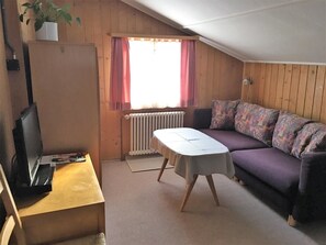 Ein gemütliches Zimmer mit einer Couch, einem kleinen Tisch, einem Heizkörper und einem Fenster mit Vorhängen.