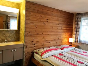 Une chambre à coucher avec une tête de lit en bois, une table de chevet avec une lampe, un lit avec une literie à motifs et une salle de bain avec un miroir et un lavabo.