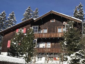 Ein mehrstöckiges Holzhaus mit einem Balkon, umgeben von schneebedeckten Bäumen.