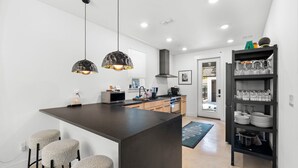 Een moderne keuken met een centraal eiland, barkrukken, hanglampen en een glasplank.