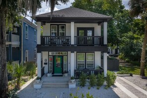 A two-story residential building with a green front door, a balcony on the upper floor, and a small front yard with plants. - The Slate Retreat | Pool + Hot Tub (Jacksonville)