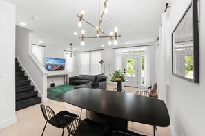 A modern living room with a dining table, black leather sofa, and a staircase.
