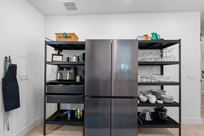 A modern kitchen with a built-in stainless steel refrigerator, multiple shelves for storage, and a variety of kitchenware. - The Slate Retreat | Pool + Hot Tub (Jacksonville)