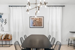 A modern dining room with a dark table, black wire chairs, a ceiling light fixture, and a framed abstract artwork. - The Slate Retreat | Pool + Hot Tub (Jacksonville)