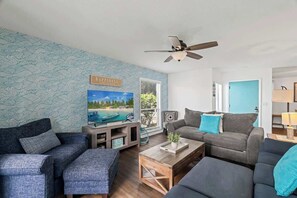 A living room with a sofa, a coffee table, a TV, and a ceiling fan. - Salt + Sun | Beach + Pool (St. Augustine)