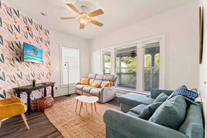 Ein Wohnzimmer mit einer Couch, einem Sessel, einem Tisch, einem Deckenventilator und einem Fenster mit Jalousien.